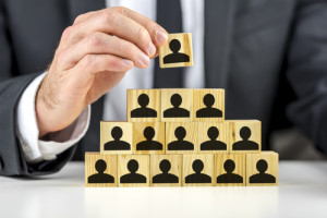 Closeup of manager hand arranging wooden cubes wit person shape in a pyramid. Concept of human resources.