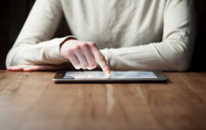 woman hand presses on screen digital tablet over wooden table