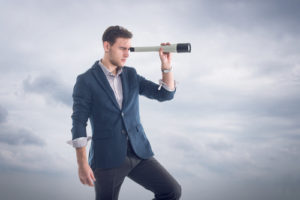 Junger Geschäftsmann, der durch ein Fernglas schaut, um neue Perspektiven zu entdecken.