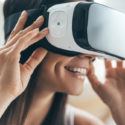 Die Zukunft ist jetzt. Attraktive junge Frau, die ihren VR-Kopfhörer justiert und beim zu Hause sitzen lächelt