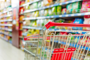 Leerer Einkaufwagen steht vor vollen Supermarktregalen