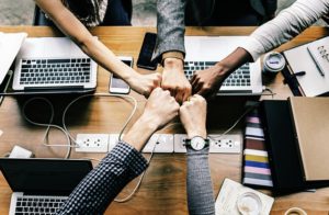 Geballte Hände, die in einem Büro neben ihren Laptops auf dem Schreibtisch aufeinandertreffen und ein Team symbolisieren