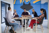 Junge Leute eines Startups im Meeting an Bürotischen und mit Laptops