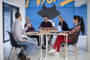 Junge Leute eines Startups im Meeting an Bürotischen und mit Laptops