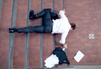 Businessmann fällt auf Treppe hin und verliert Aktentasche mit Papieren