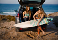 Zwei Surferinnen mit Surfbrett und Auto