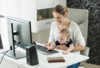 Frau arbeitet mit Baby am Computer Zuhause