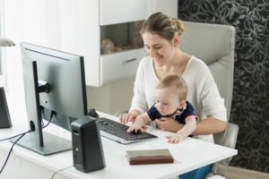 Frau arbeitet mit Baby am Computer Zuhause