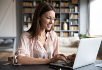 Junge Frau sitzt am Schreibtisch vor einem Laptop im Home-Office