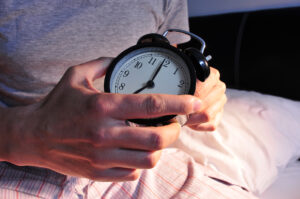 Junger Mann im Bett mit Wecker in der Hand