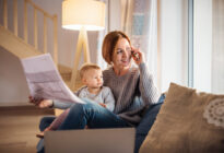 Homeoffice: Junge Mutter, die mit Tochter auf Schoss von Zuhause arbeitet