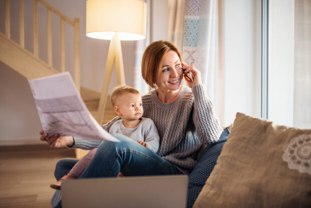 Homeoffice: Junge Mutter, die mit Tochter auf Schoss von Zuhause arbeitet