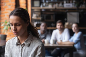 Frau im Café schaut betrübt, im Hintergrund gaffen drei Personen