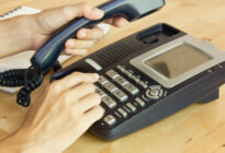 Hand wählt auf Tastentelefon, das auf einem Schreibtisch steht, Telefonnummer