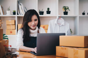Junge, asiatische Frau sitzt vor Laptop mit vielen Paketen