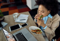 Geschäftsfrau isst Sandwich während eines Onlinemeetings im Büro