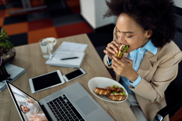 Geschäftsfrau isst Sandwich während eines Onlinemeetings im Büro