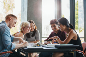 Mehrere weibliche und männliche Studenten diskutierend und schreibend am Tisch