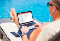 Businessmann sitzt mit Laptop am Pool im Liegestuhl