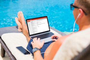 Businessmann sitzt mit Laptop am Pool im Liegestuhl