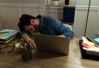 Junger Mann schläft am Schreibtisch neben Laptop