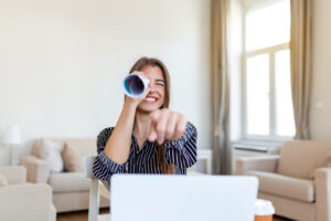 Lächelnde junge Geschäftsfrau schaut durch Papierrolle am Schreibtisch im Home-Office