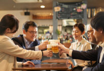 Zwei Asiatische Geschäftsfrauen und drei asiatische Geschäftsmänner prosten sich mit Bier in einem Lokal zu
