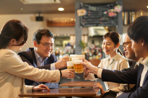 Zwei Asiatische Geschäftsfrauen und drei asiatische Geschäftsmänner prosten sich mit Bier in einem Lokal zu