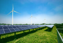 Solarpanels und Windkraftwerke vor blauem Himmel auf grüner Wiese