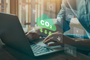 Männerhände an Laptop, darüber ist Schild mit Aufschrift CO2 Reduktion