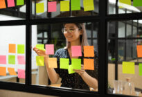 Junge Frau hängt Post-Its an Fenster im Büro