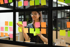 Junge Frau hängt Post-Its an Fenster im Büro