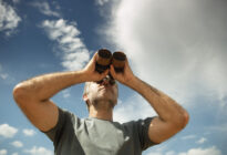 Mann blickt mit Fernglas in den Himmel