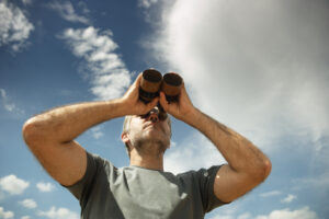 Mann blickt mit Fernglas in den Himmel