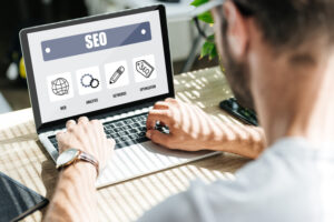 Mann tippt in Laptop mit Computerbildschirm, auf dem SEO steht