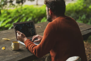 Mann sitzt gemütlich am Holztisch in der Natur an seinem Laptop