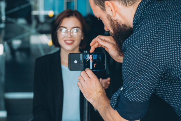 Männlicher Assistent, der ein Interview mit einer Geschäftsfrau mit dem Smartphone aufnimmt.