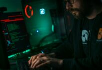 Ein Mann mit Brille in einem dunklen Raum vor einem Computer mit leuchtenden grünen Lichtern.