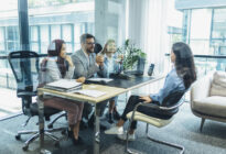 Bewerberin sitzt vor drei Businessleuten am Schreibtisch zum Gespräch