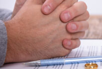 Eine Frauen- und eine Männerhand liegen auf einem Vertrag, daneben sind ihre Eheringe und ein Kugelschreiben