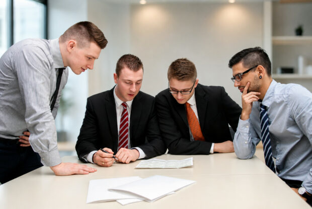 Vier Geschäftsleute prüfen gemeinsam Unterlagen bei einer Besprechung zum Compliance-Outsourcing im Mittelstand.